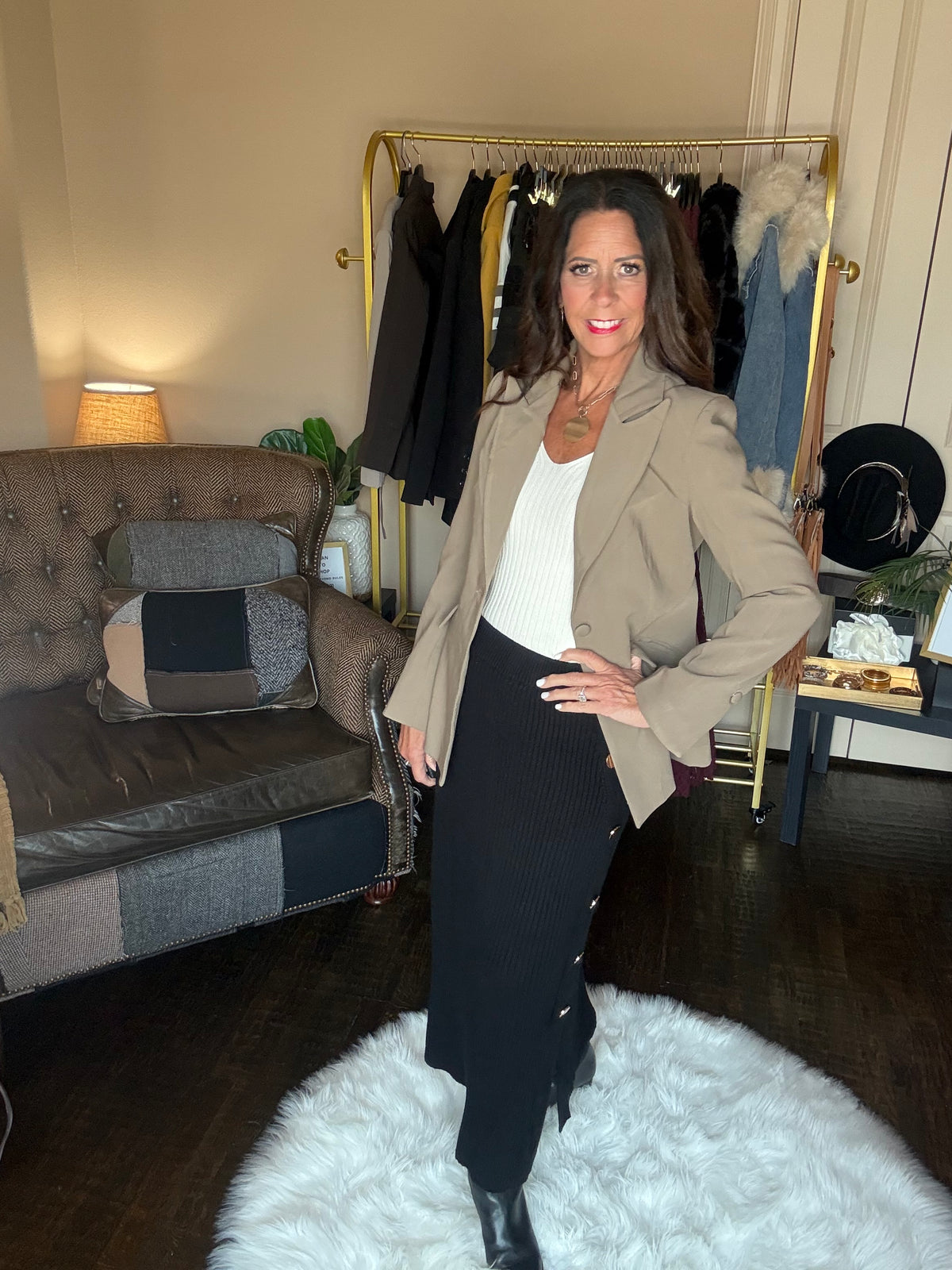 Model is wearing a khaki blazer with a cream top, black ribbed maxi skirt with gold button details, and black booties