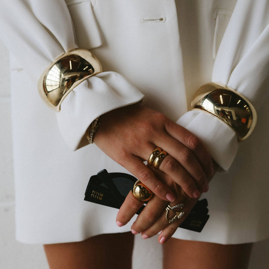 Close-up of hands wearing gold cuffs and rings, with a white suit jacket.