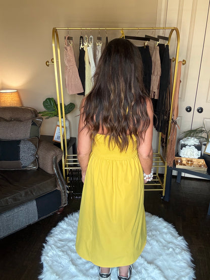 Person wearing a yellow dress standing in a room with a gold rack and white rug.