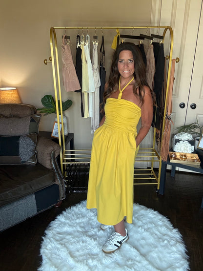 Woman in a yellow dress standing in front of a mirror in a room with a white rug and gold bar cart.