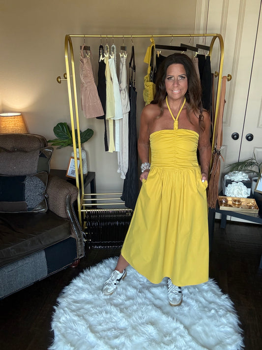 Woman in a yellow dress standing in front of a mirror in a room with a white rug and furniture.