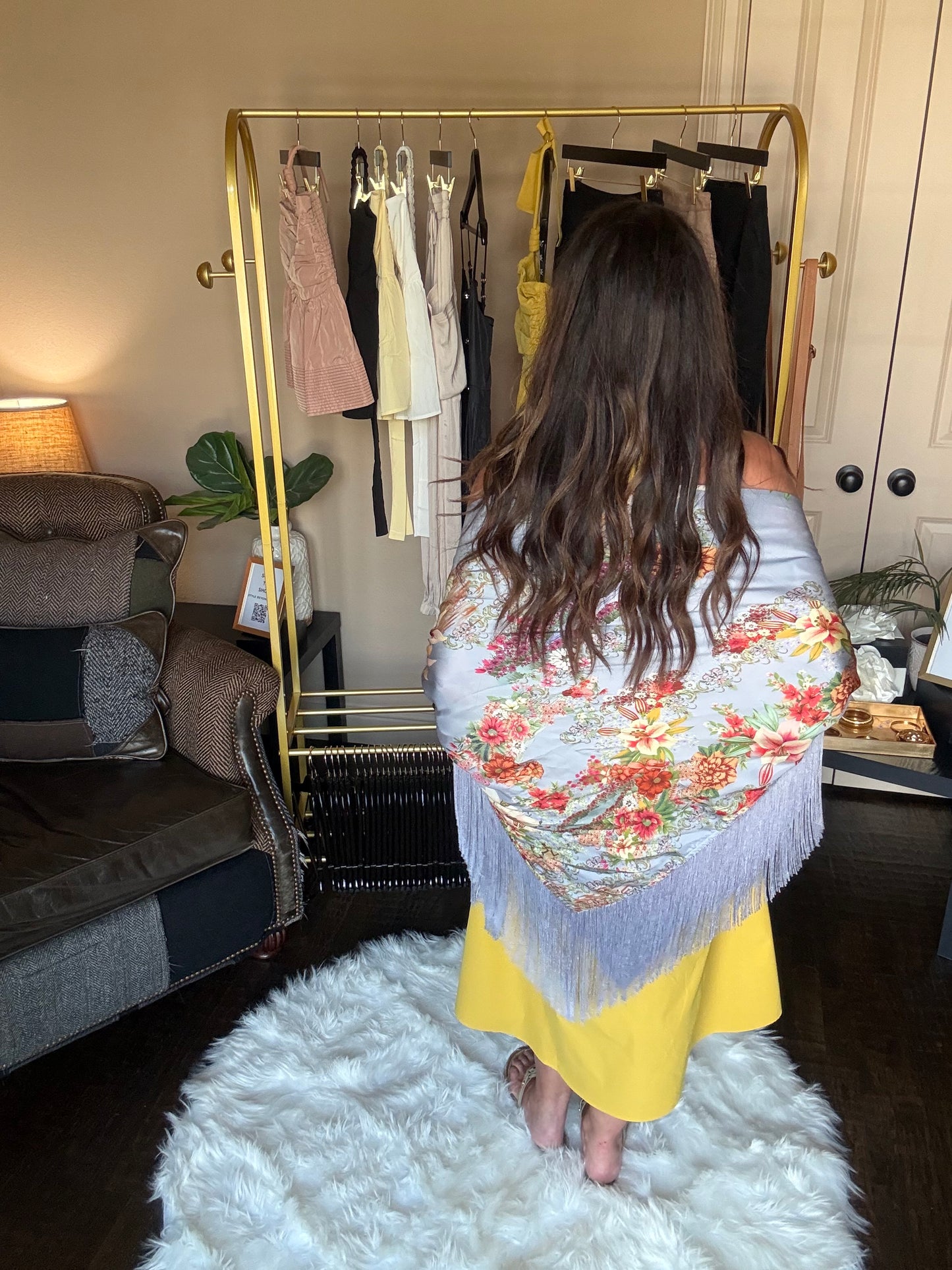 Person wearing a floral headscarf and yellow outfit standing in a room with a mirror and white rug.
