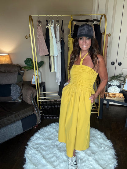 Woman in a yellow dress modeling in front of a mirror in a room with a white rug and furniture.
