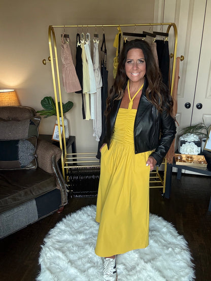 Woman in a yellow dress and black leather jacket standing in a room with a gold bar cart and white rug.
