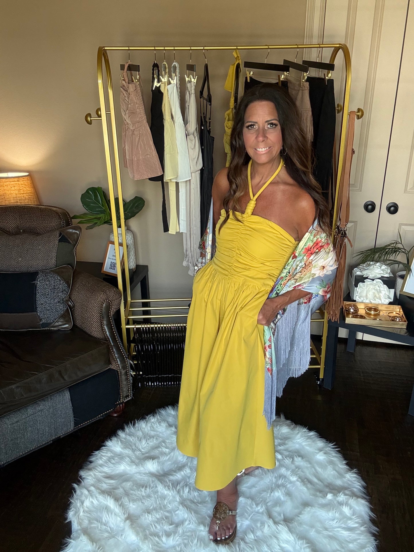 Woman in a yellow dress standing in front of a mirror in a room with a white rug and furniture.
