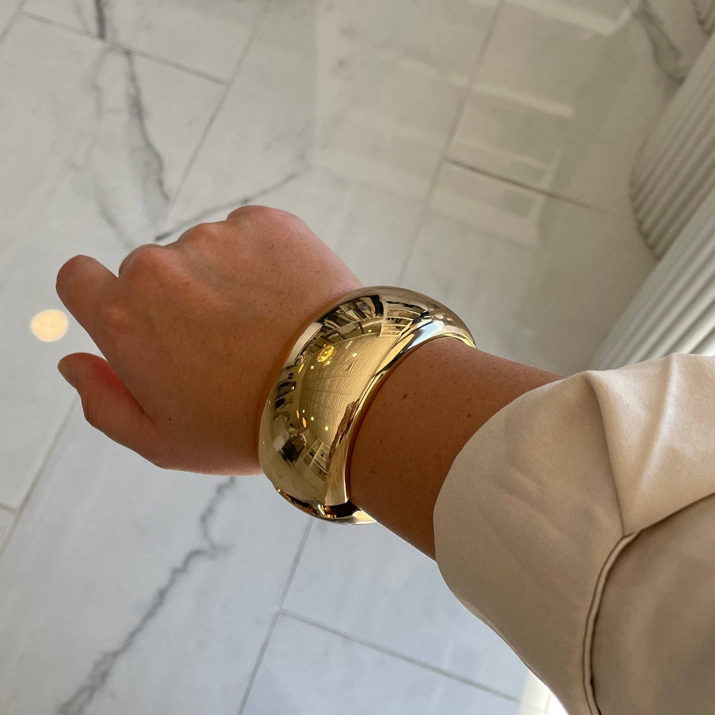 Gold bracelet on a wrist with a neutral background