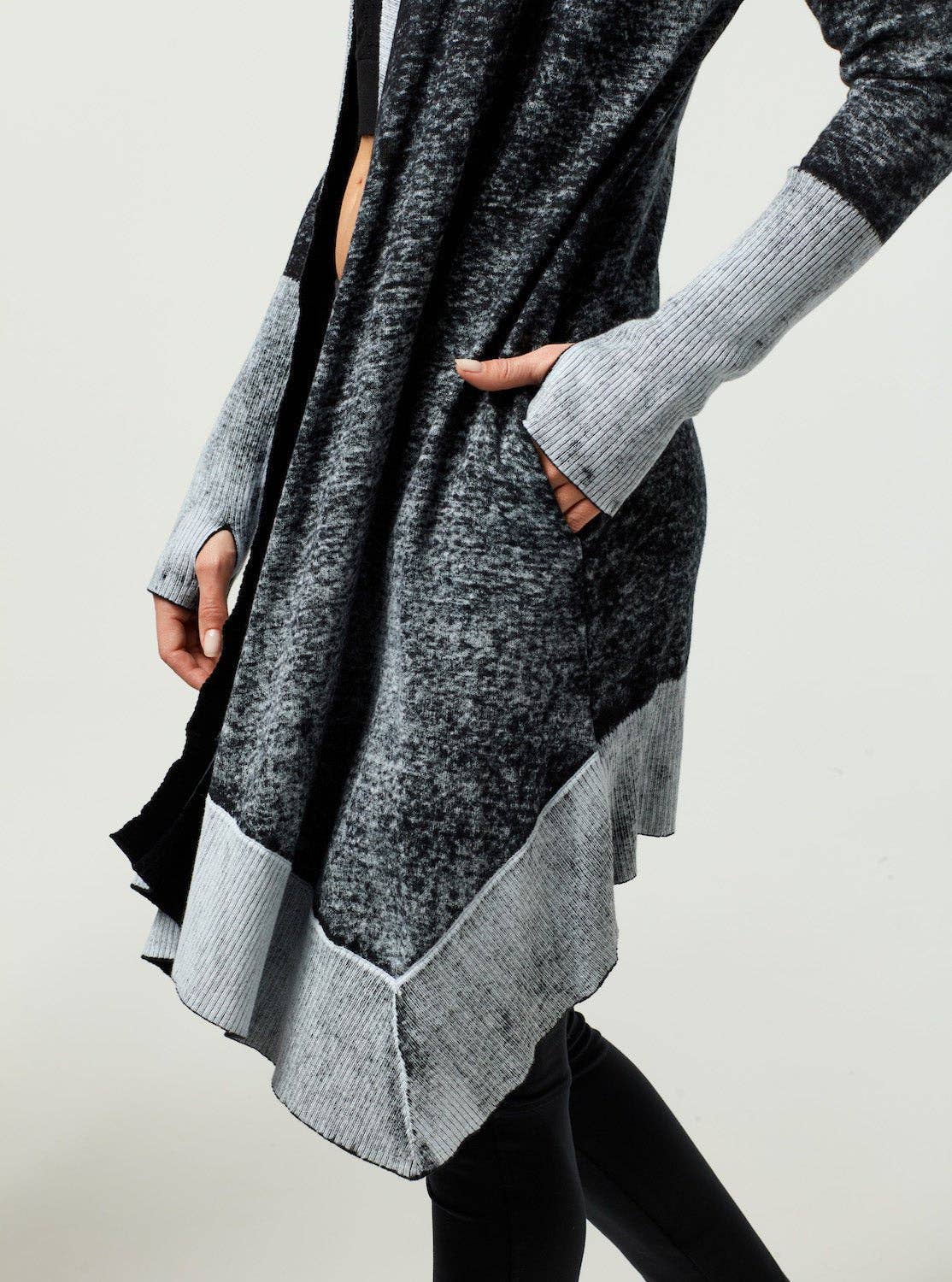Person wearing a gray and black long sweater with a plain background