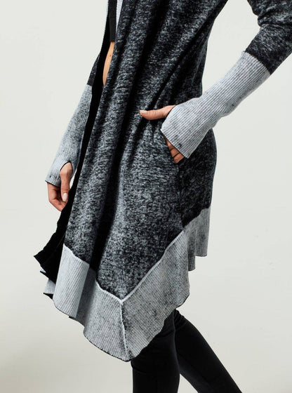 Person wearing a gray and black long sweater with a plain background