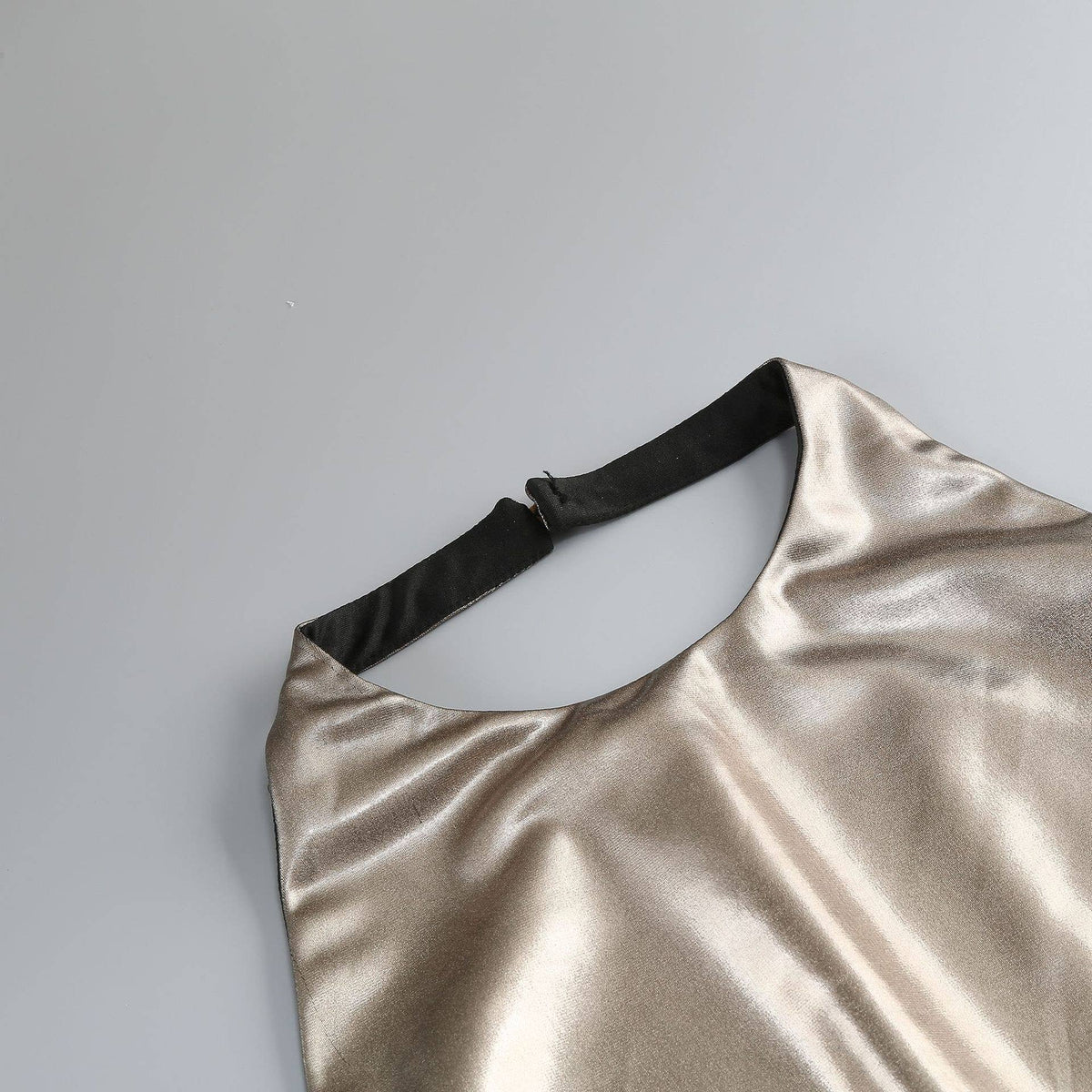 Gold metallic dress with black strap on a light gray background