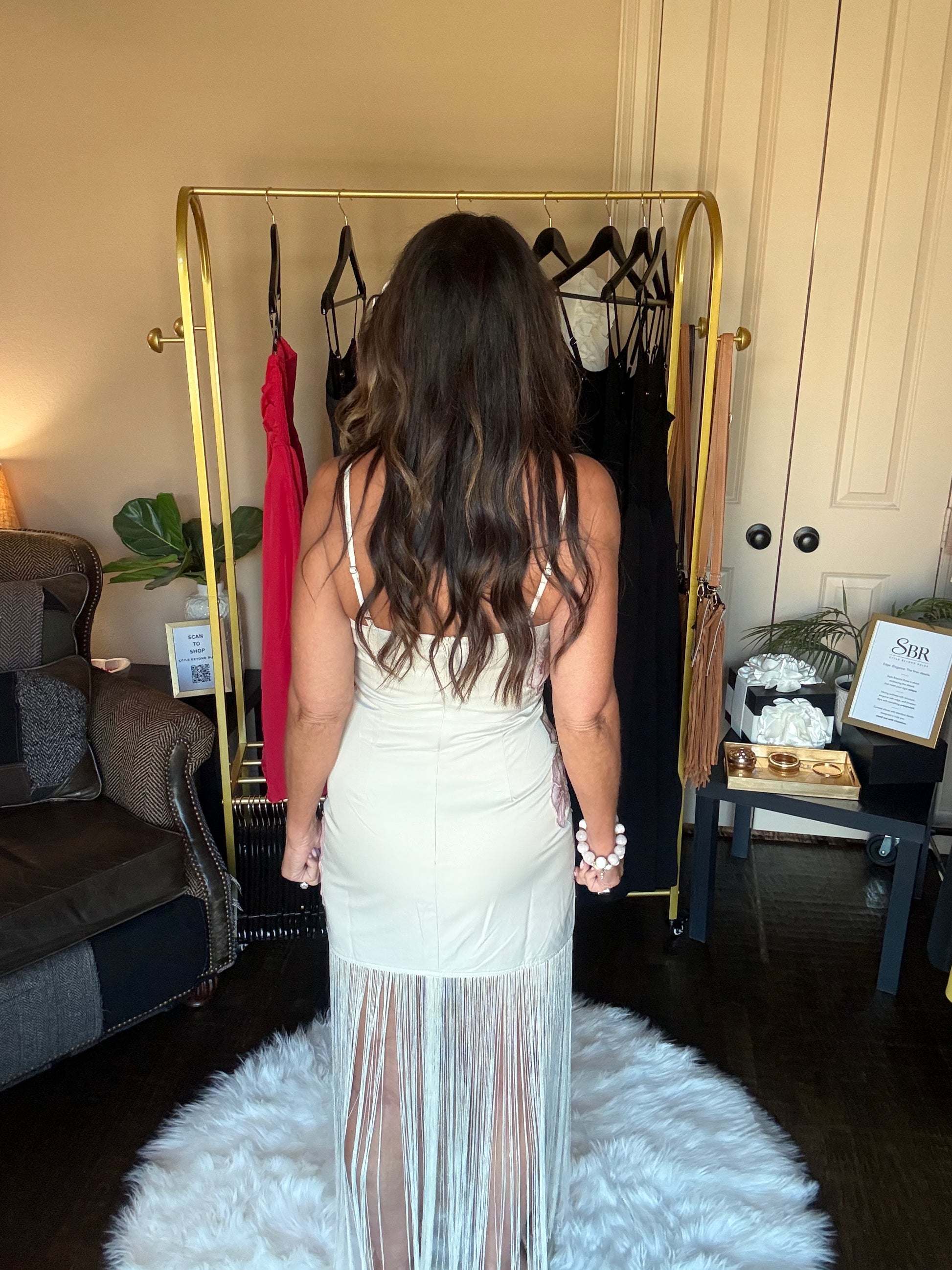 Woman in a white dress standing in front of a gold clothing rack with dresses on it.