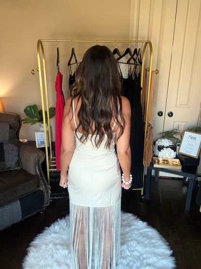 Woman in a white dress standing in front of a gold clothing rack with dresses on it.
