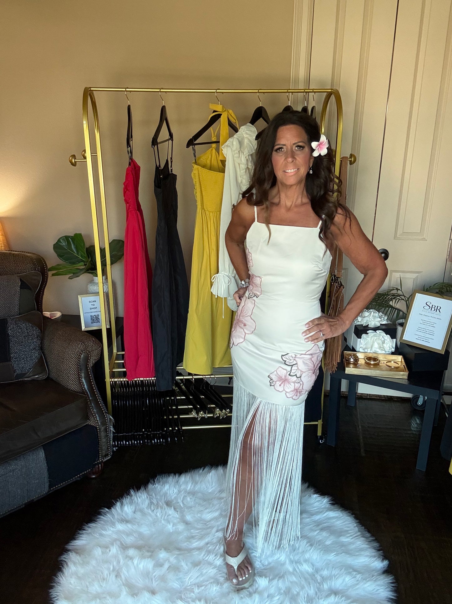 Woman in a white dress standing in a room with a rack of dresses in the background.