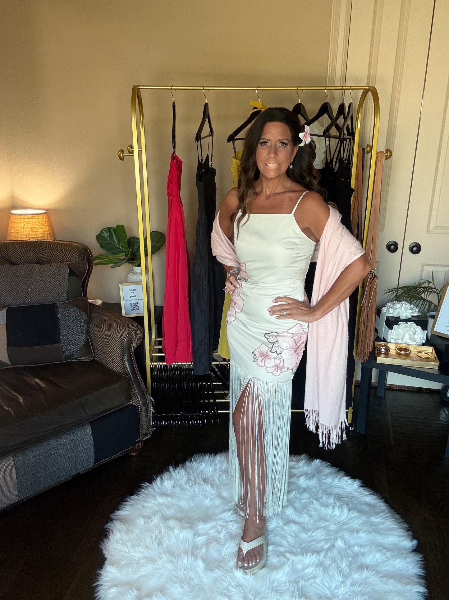 Woman in a white dress with sheer panels standing in a room with a clothing rack and furniture.