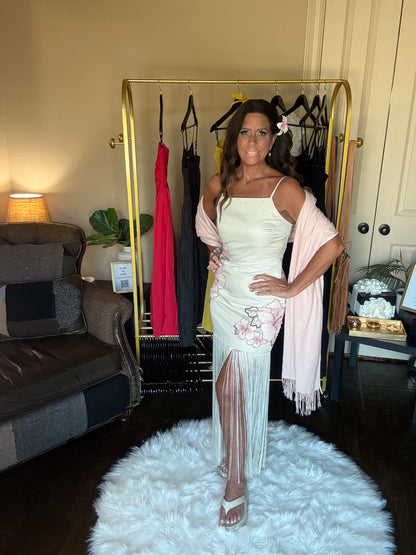 Woman in a white dress with sheer panels standing in a room with a clothing rack and furniture.
