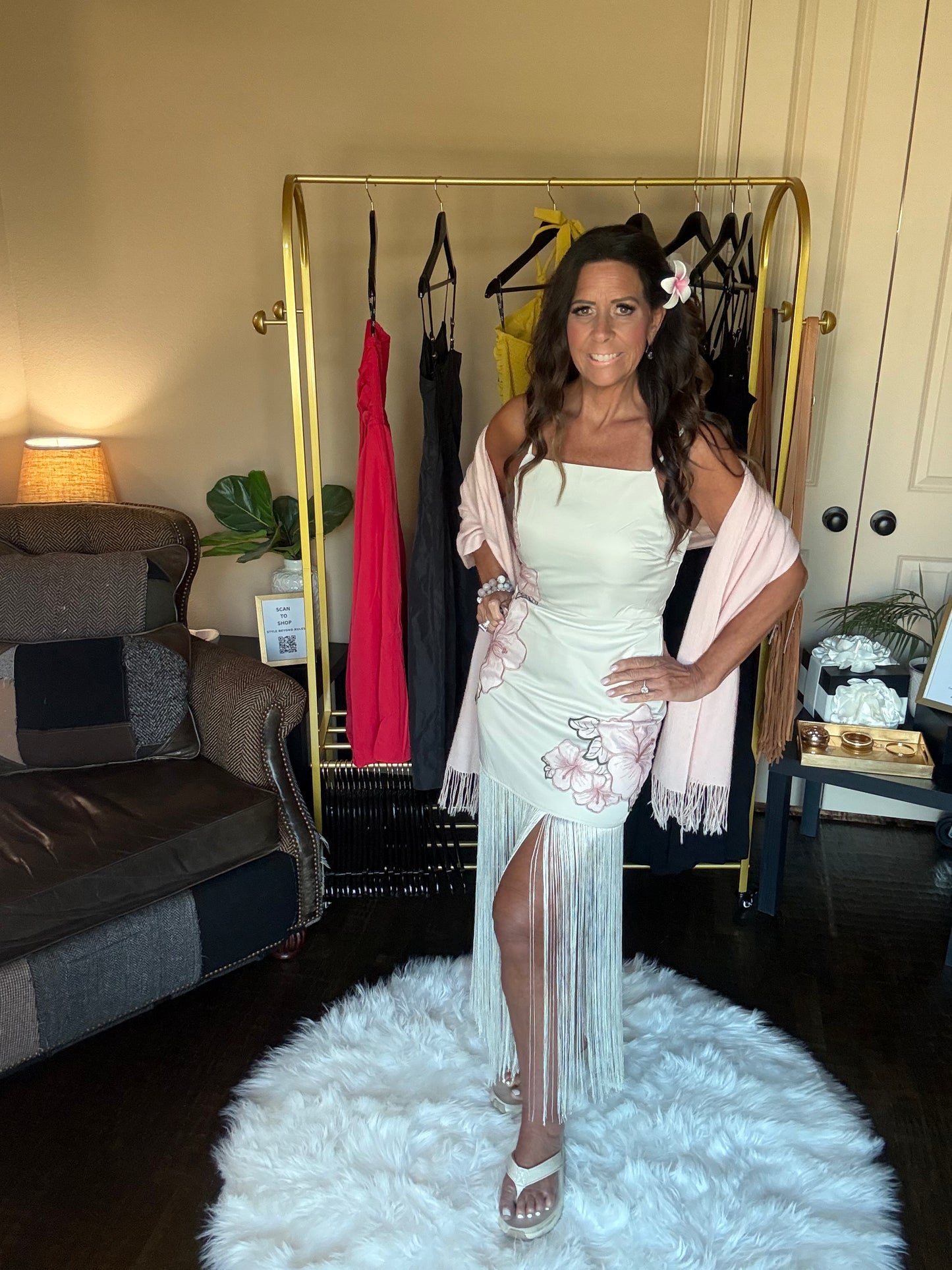 Woman in a light-colored dress with floral details standing in a room with clothing racks and furniture.