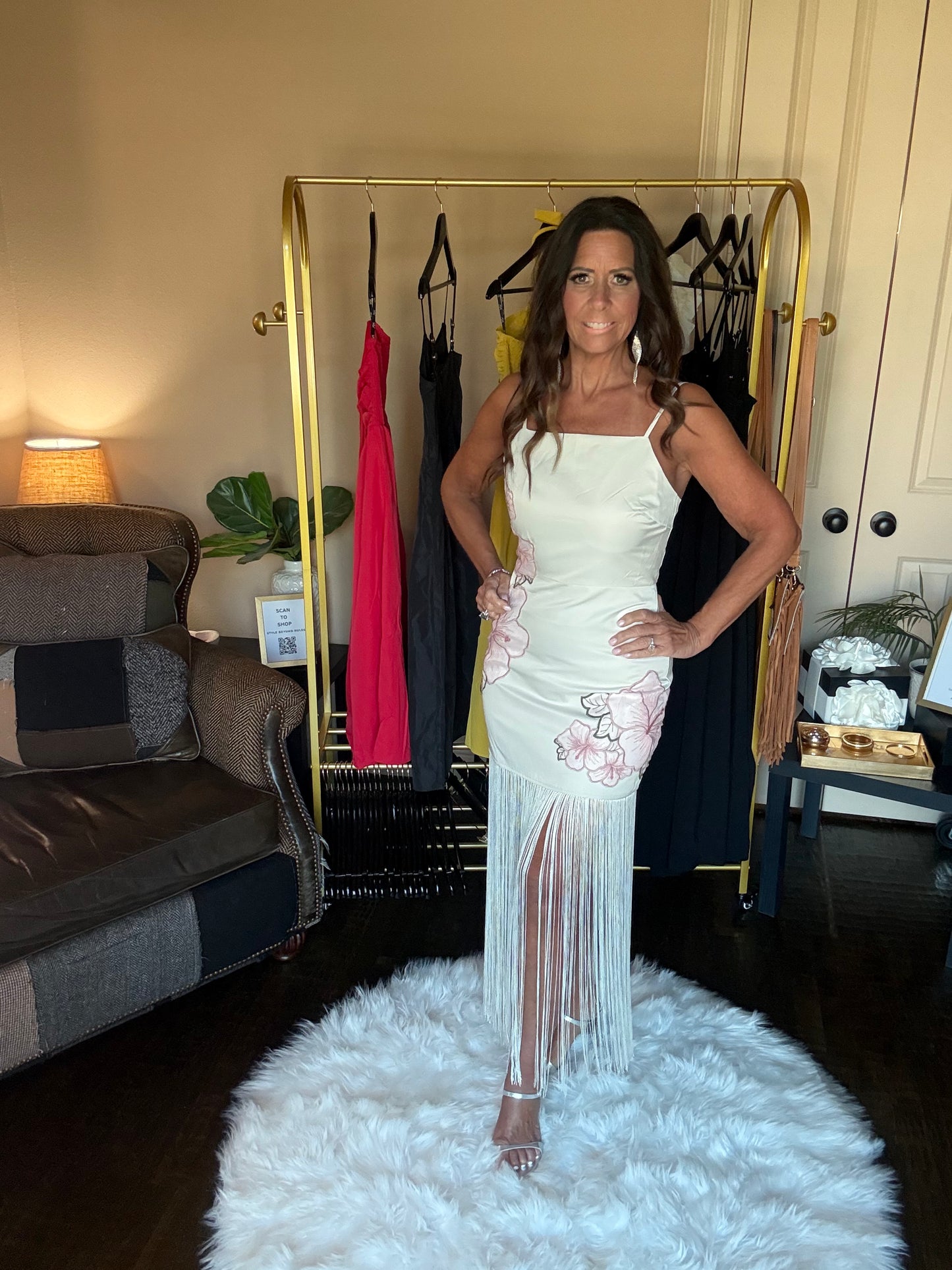 Woman in a white dress standing in a room with a rack of clothes and a couch.