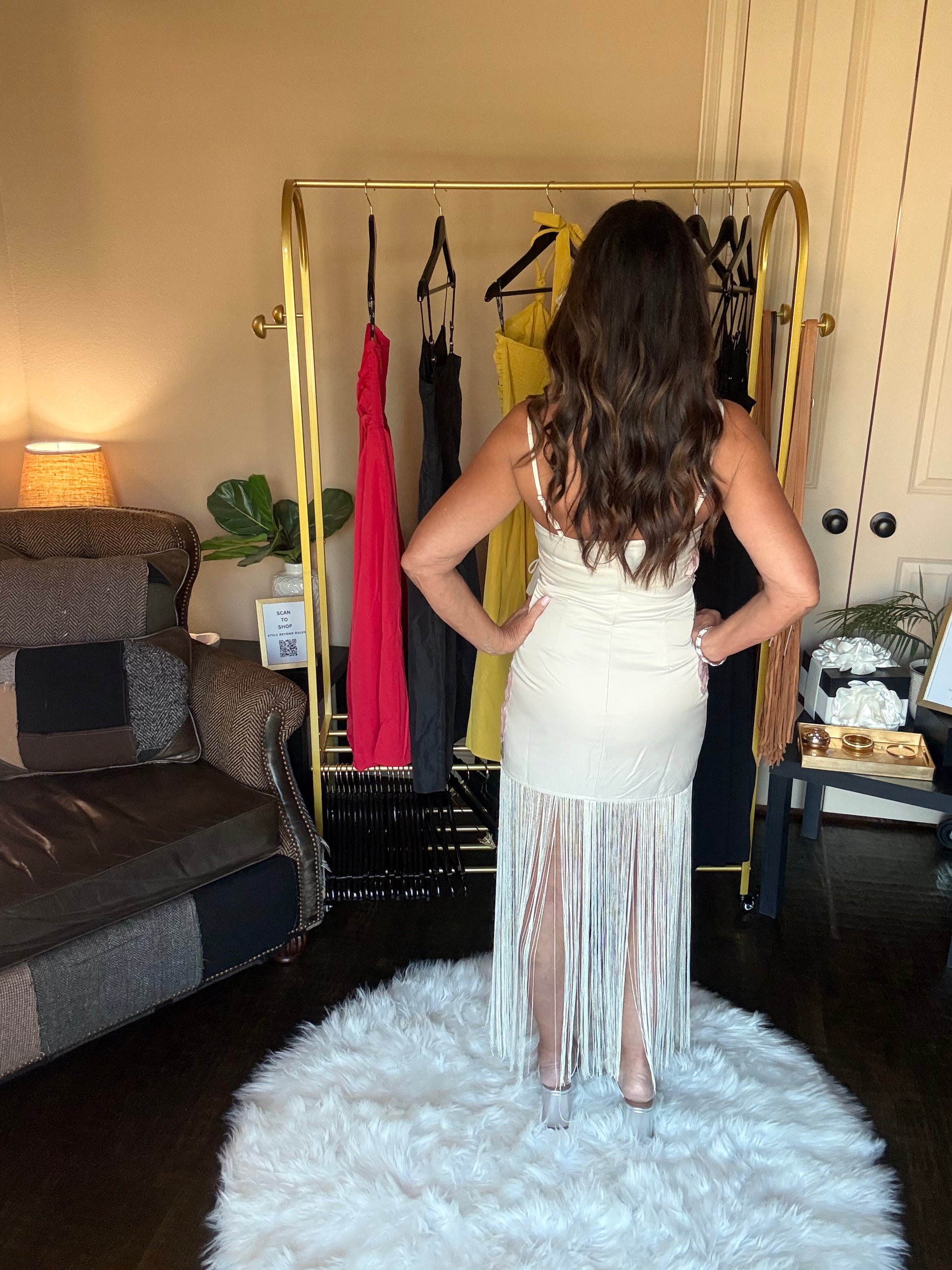 Woman in a white fringe dress standing in front of a clothing rack with various dresses.