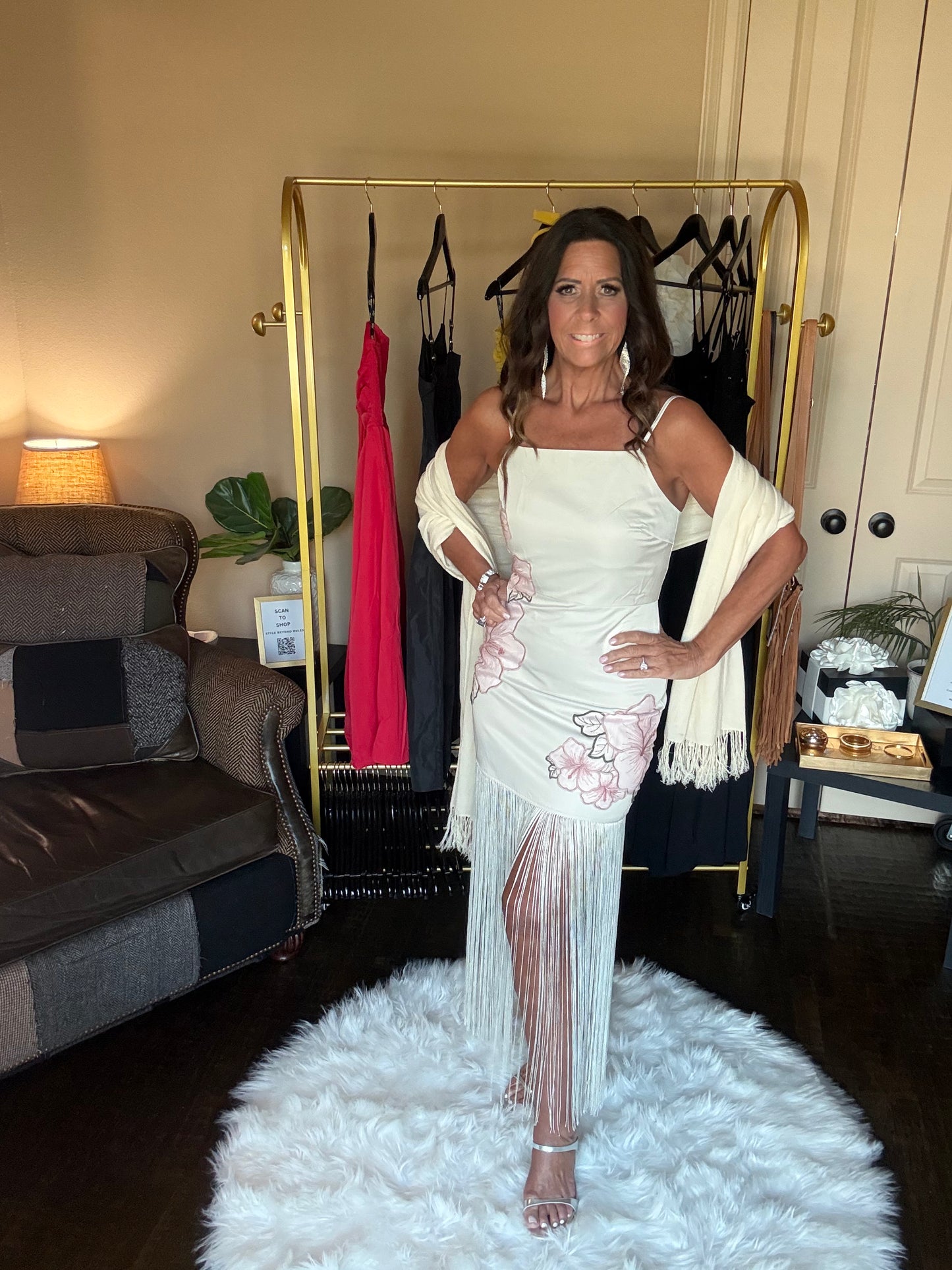 Woman in a white dress standing in a room with a clothing rack and furniture.