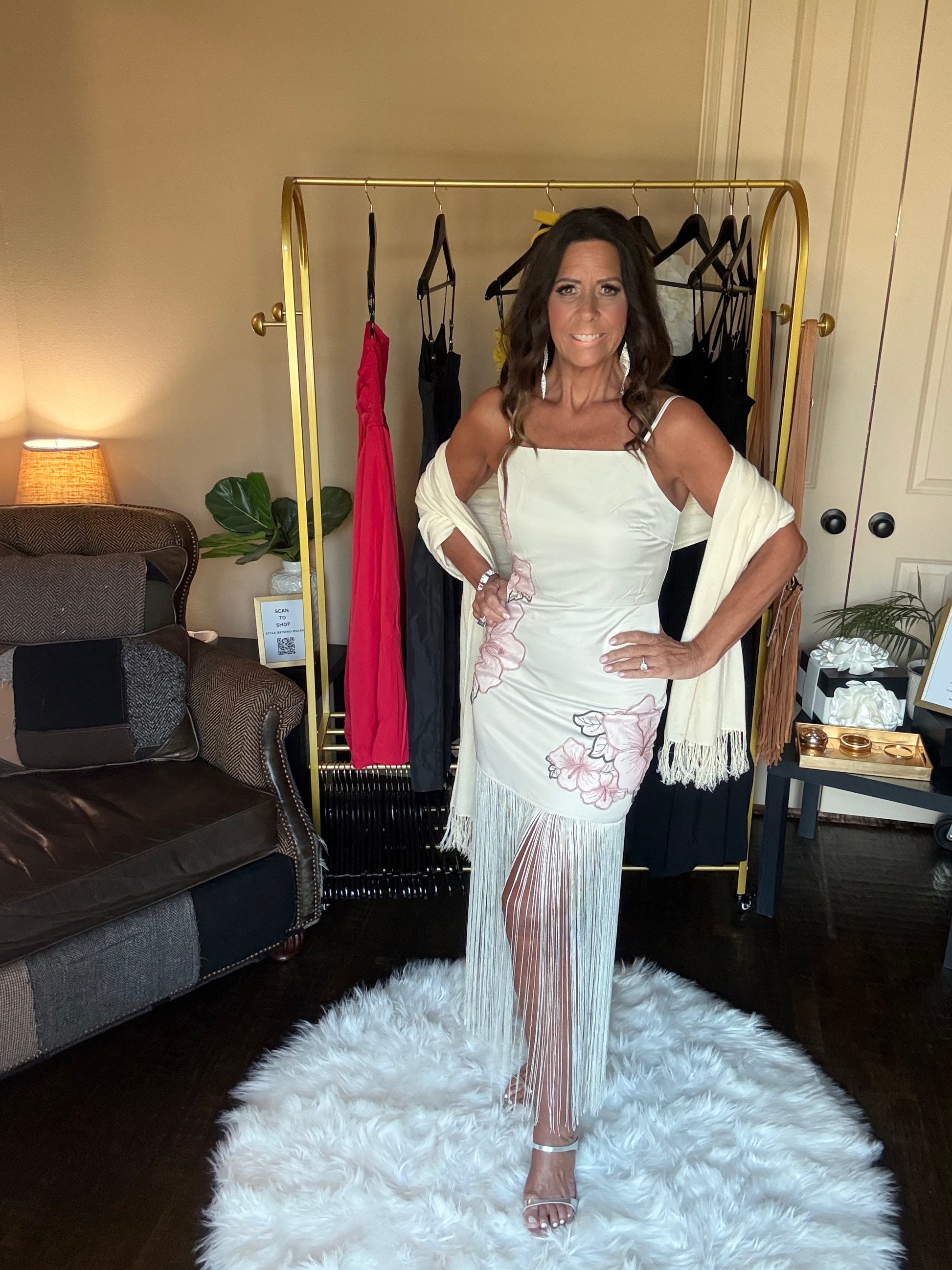 Woman in a white dress standing in a room with a clothing rack and furniture.