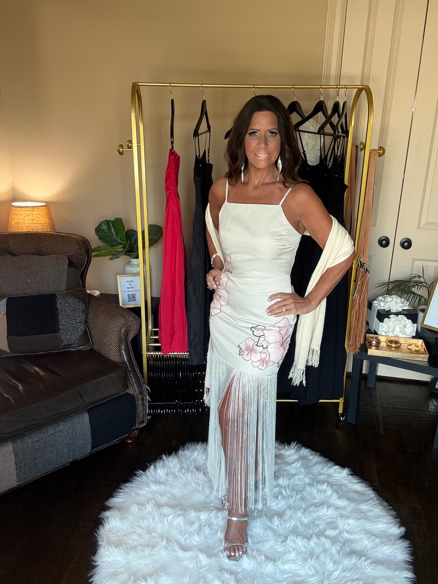 Woman in a white dress standing on a white rug in a room with a gold rack and clothing.