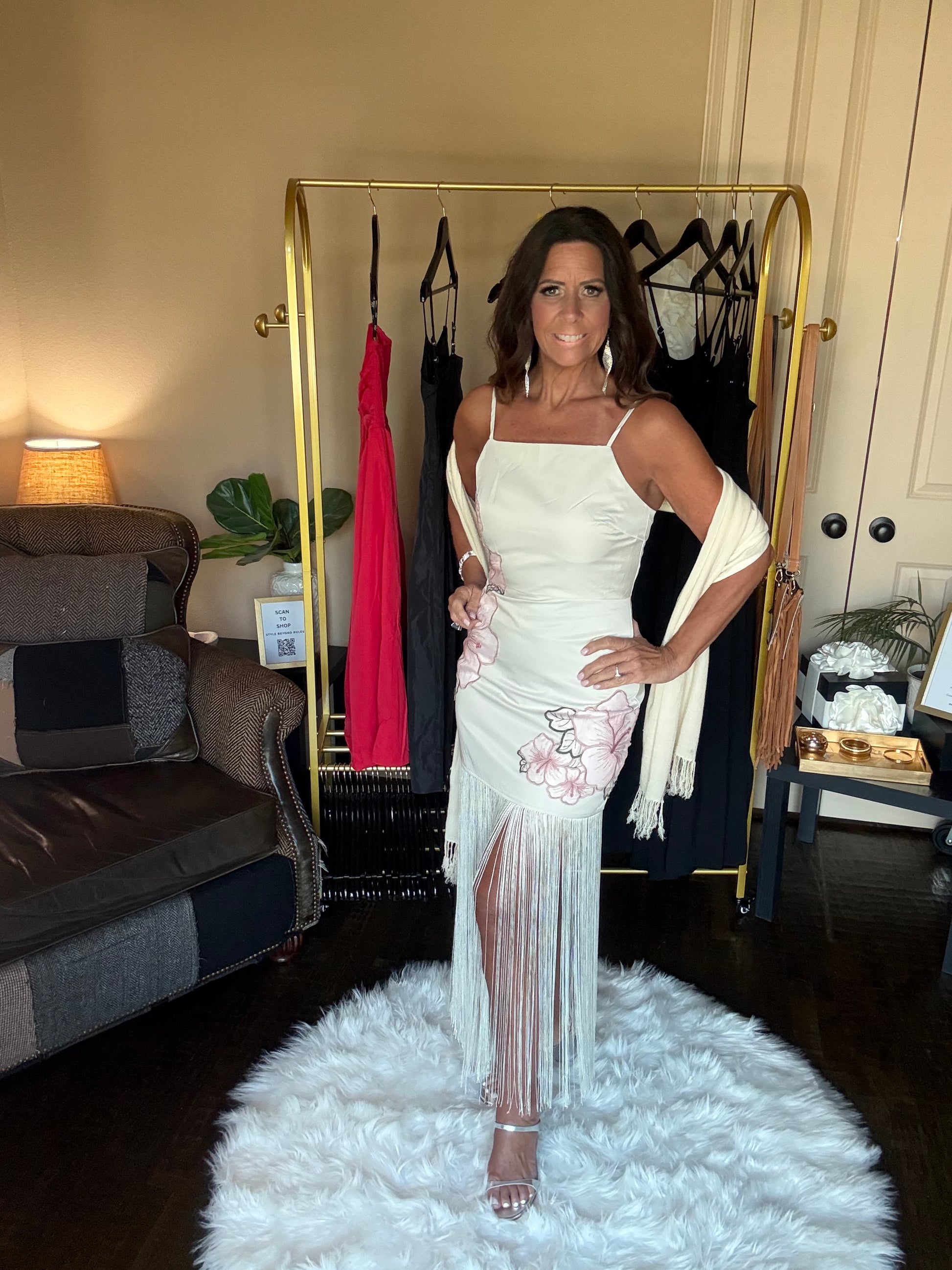 Woman in a white dress standing on a white rug in a room with a gold rack and clothing.