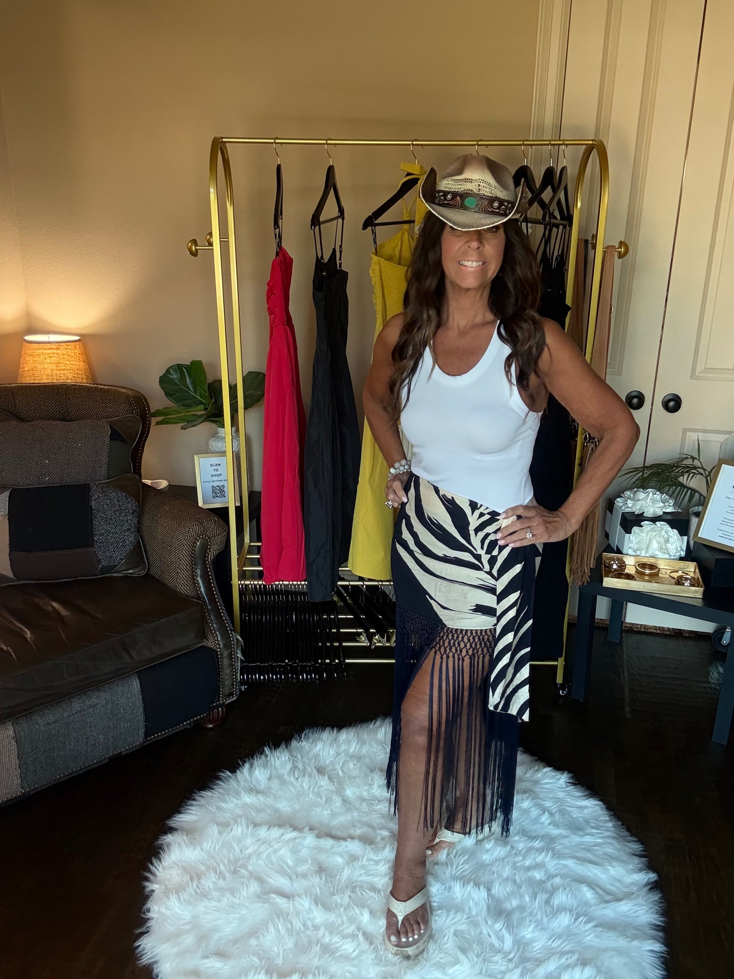 Woman posing in a room with a clothing rack and furniture.