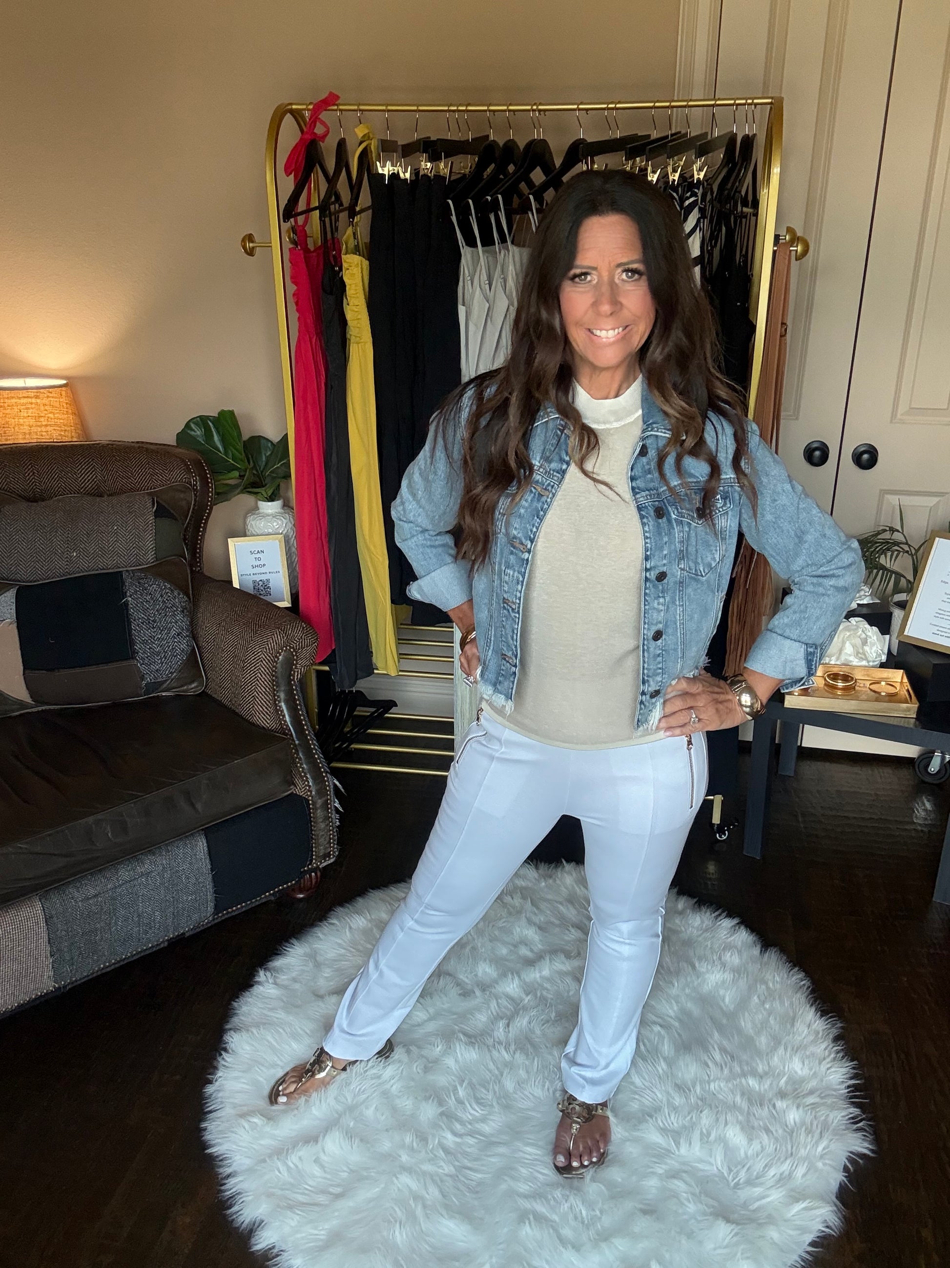 Woman standing in a room with a mirror, clothing rack, and white rug.