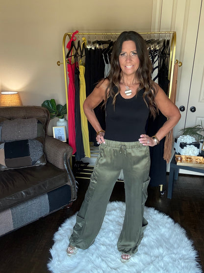 Woman holding up a pair of green pants in a room with furniture and decor.