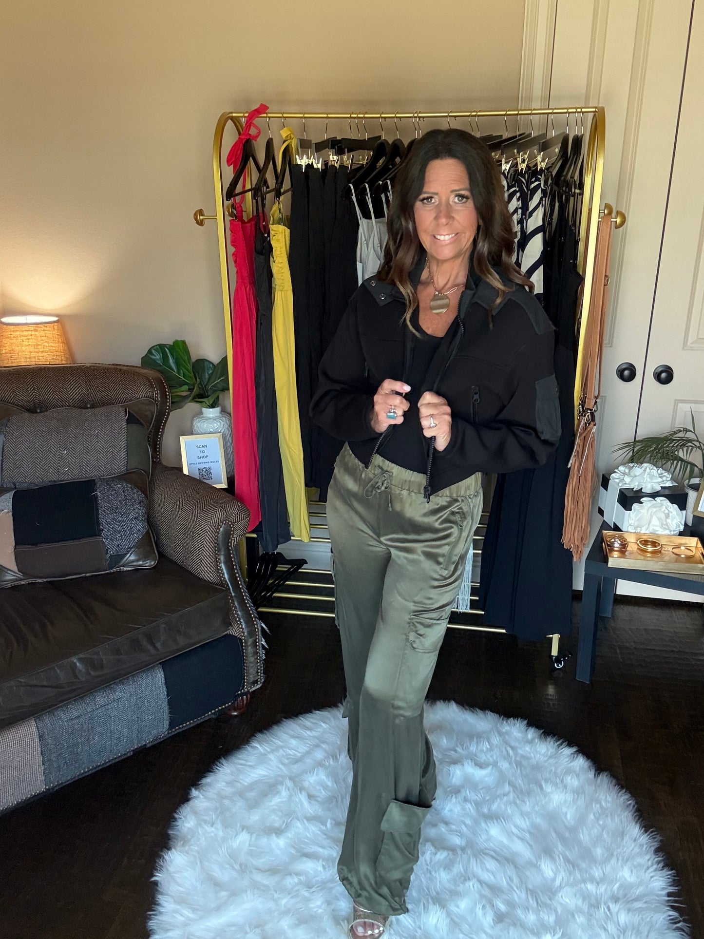 Person standing in front of a mirror with a rack of clothes and a suitcase on the floor.