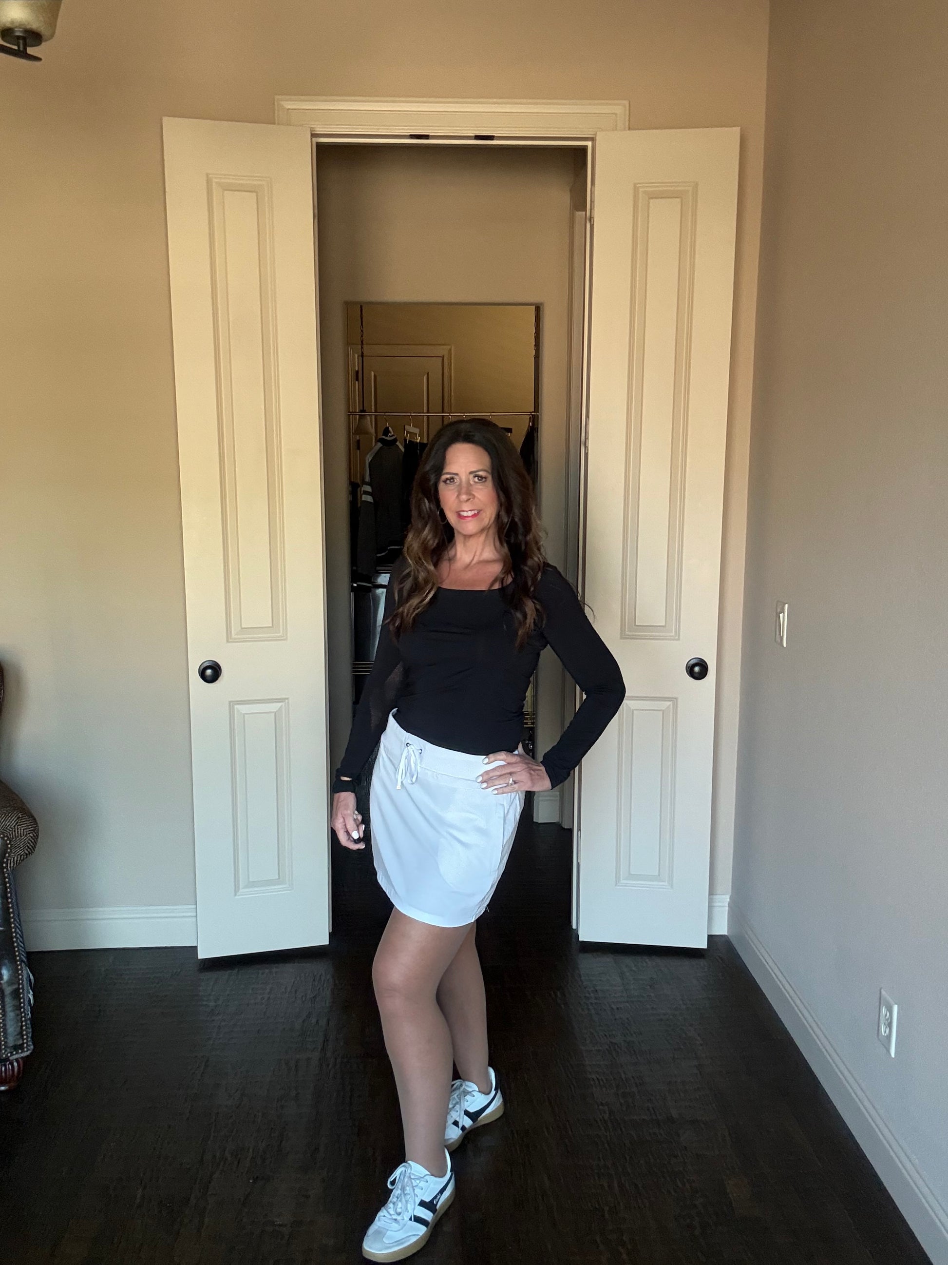 Woman standing in a doorway wearing a black top and white skirt.
