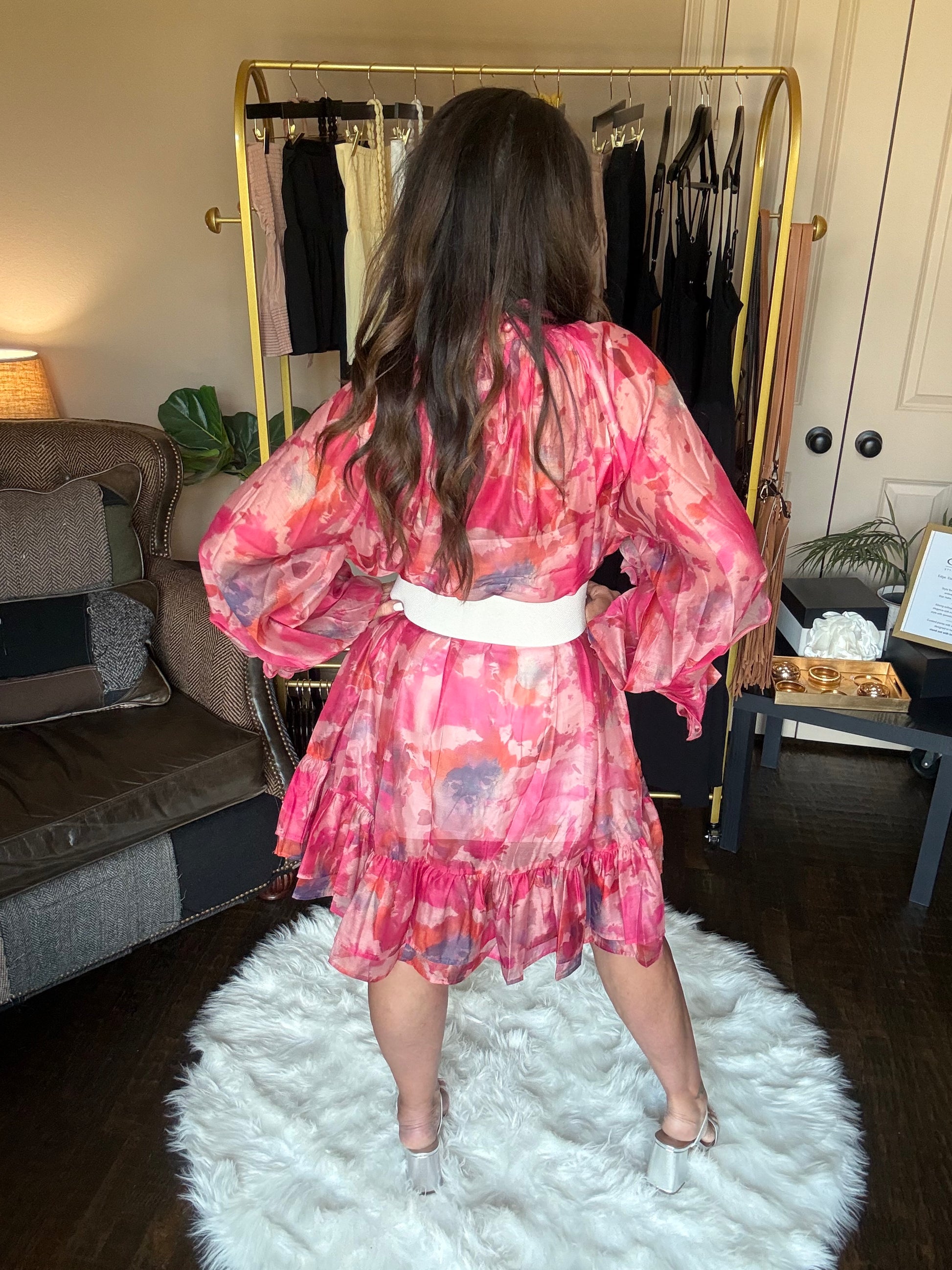Person wearing a pink floral dress standing in a room with a mirror and white rug.