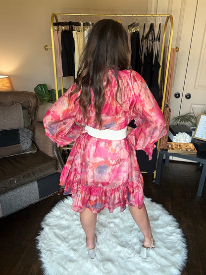 Person wearing a pink floral dress standing in a room with a mirror and white rug.