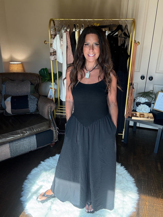 Woman wearing a black top and gray skirt standing in a room with a clothing rack.