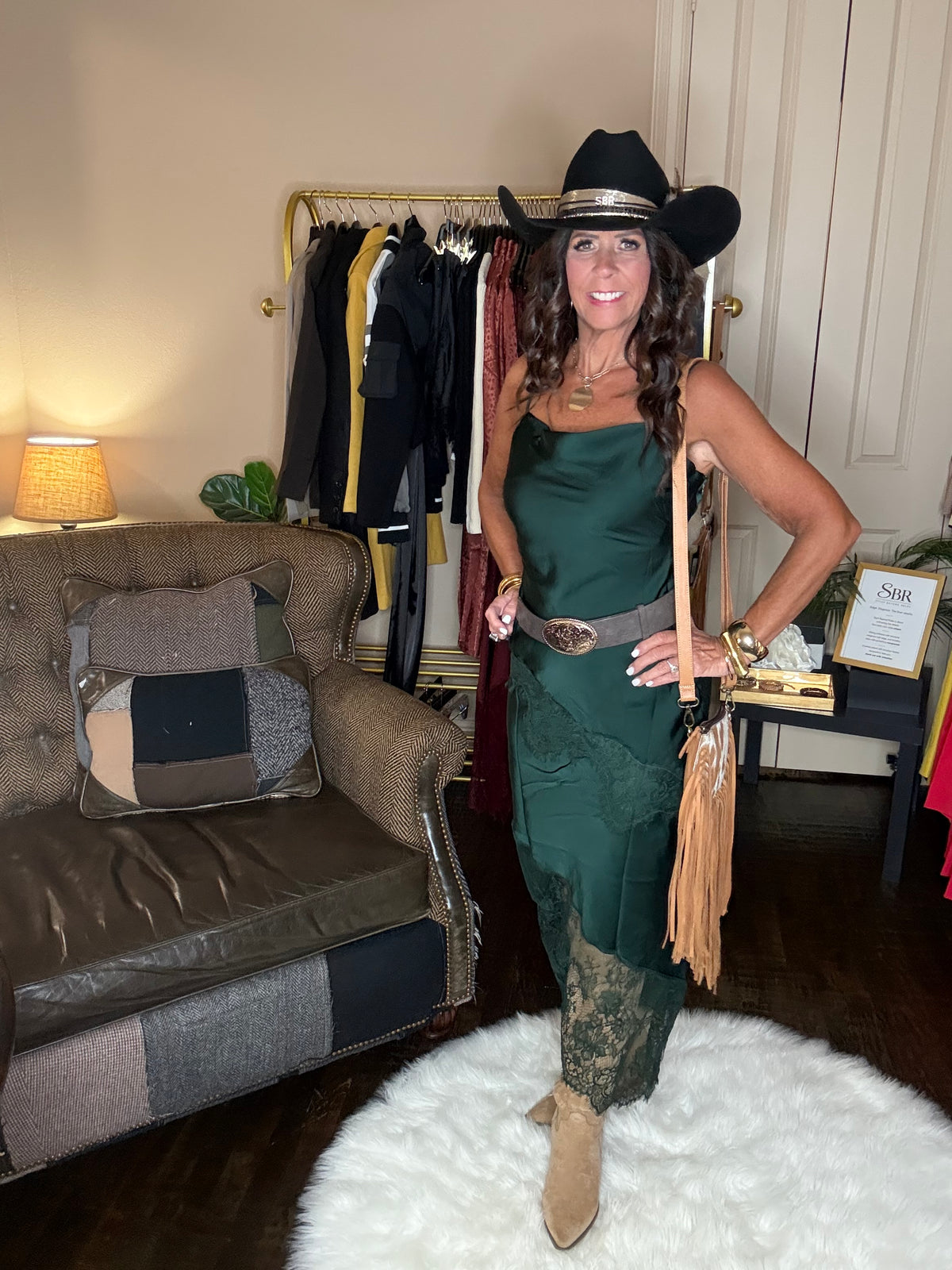 Model is wearing a hunter green satin and lace maxi dress with spaghetti straps and an asymmetrical hem and a cowboy chic vibe.