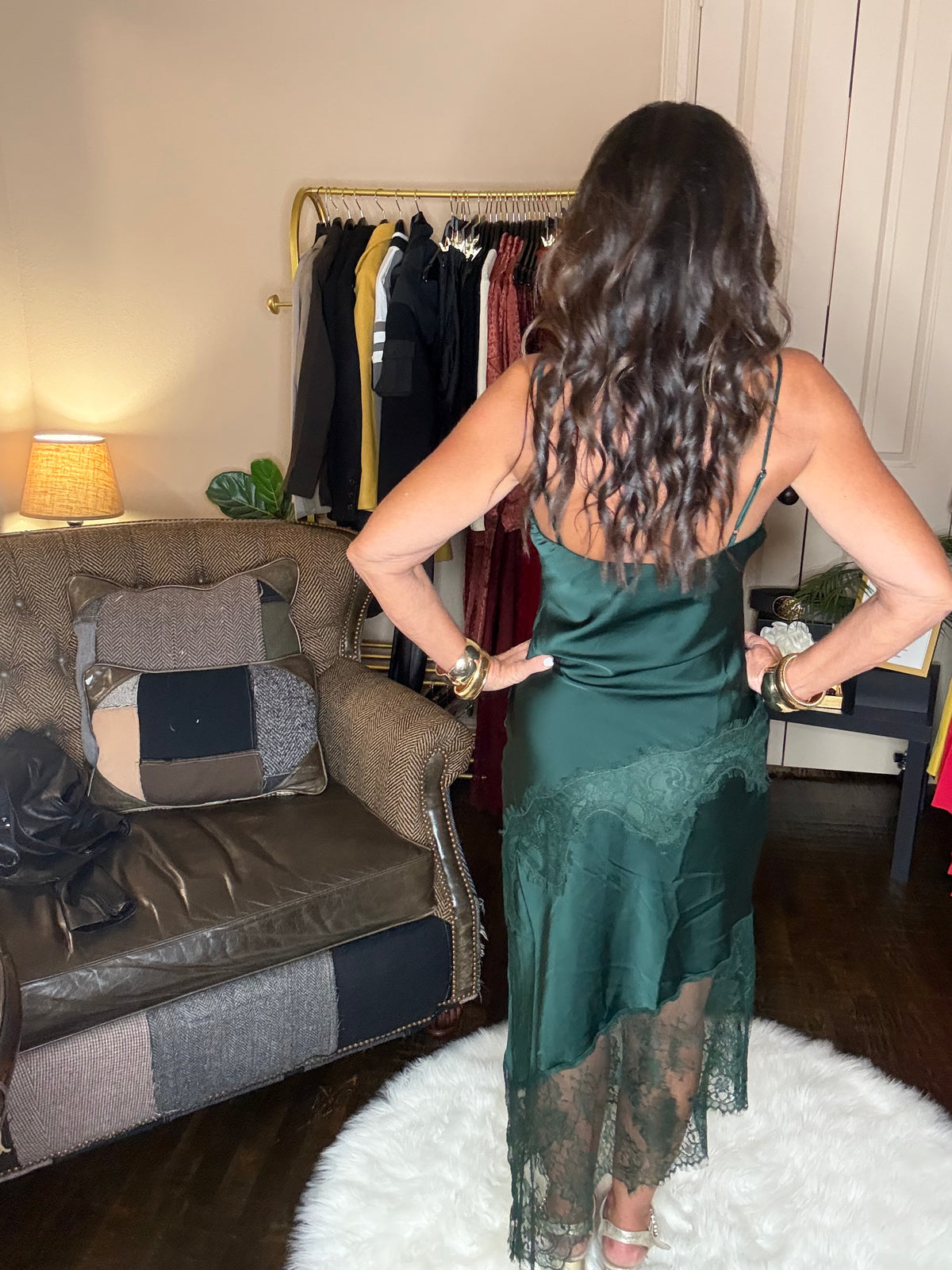 Model is wearing a hunter green satin and lace maxi dress with spaghetti straps and an asymmetrical hem land gold metallic heels.