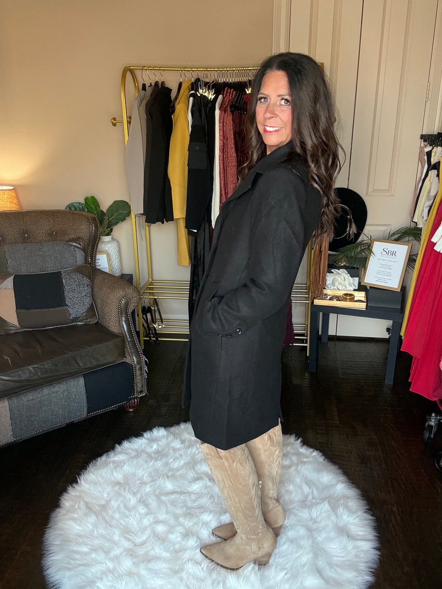 Model is wearing a black mid length coat and tall suede boots.