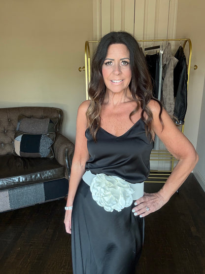 Woman holding a black evening gown with a white flower detail in a room.