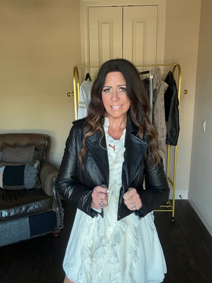 woman wearing a white ruffle dress and a back leather jacket