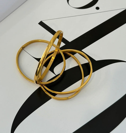 four thin gold bracelets in a random scattered display on a black and white table