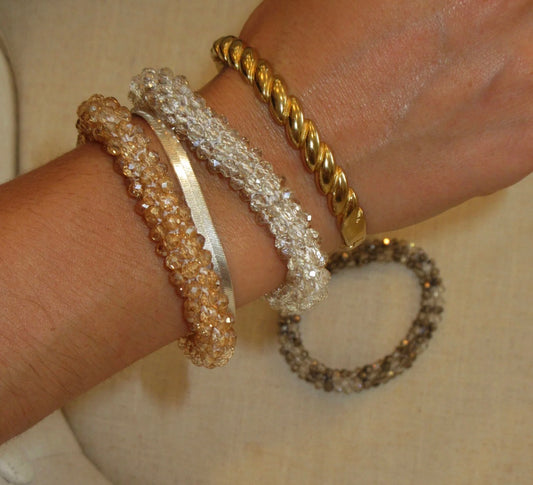 Three gold bracelets on a wrist against a neutral background
