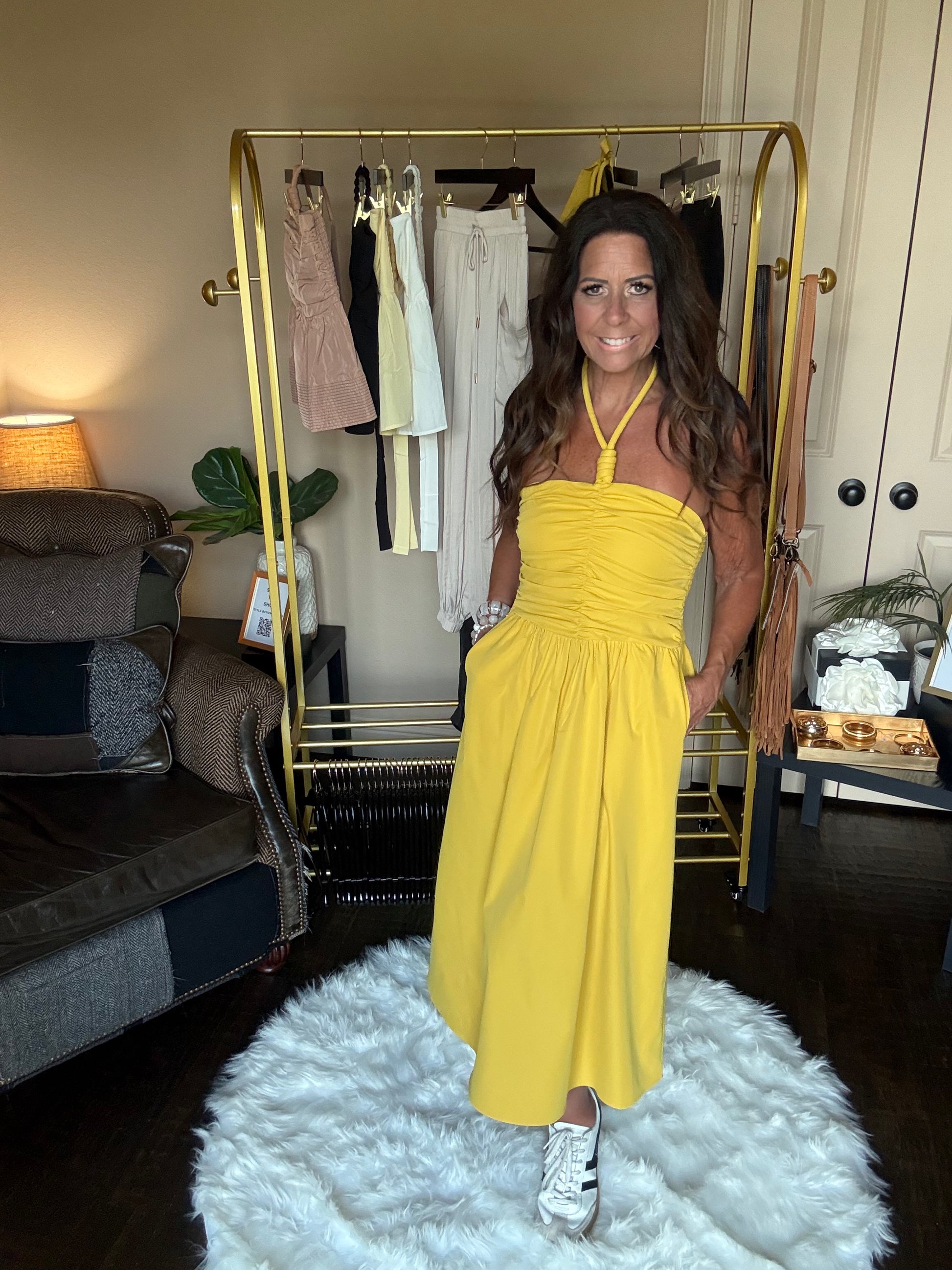 Woman in a yellow dress standing in a room with a clothing rack and furniture.