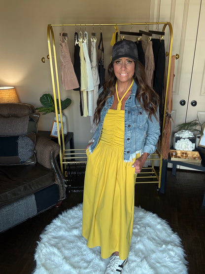 Woman in yellow dress and denim jacket standing in a room with a clothing rack.