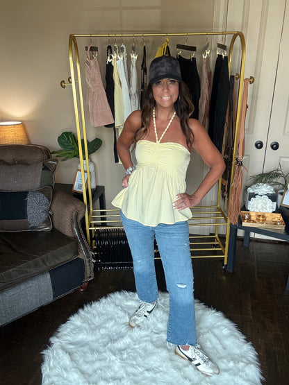 Woman in a yellow top and blue jeans standing in a room with a gold mirror and white rug.