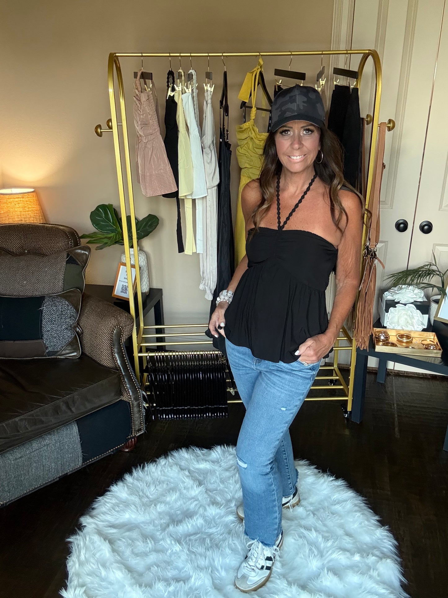 Person standing in a room with a gold bar cart, clothing rack, and white rug.