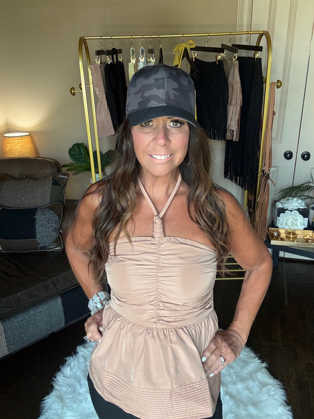 Woman in a beige top posing in a room with a mirror and decorative items.