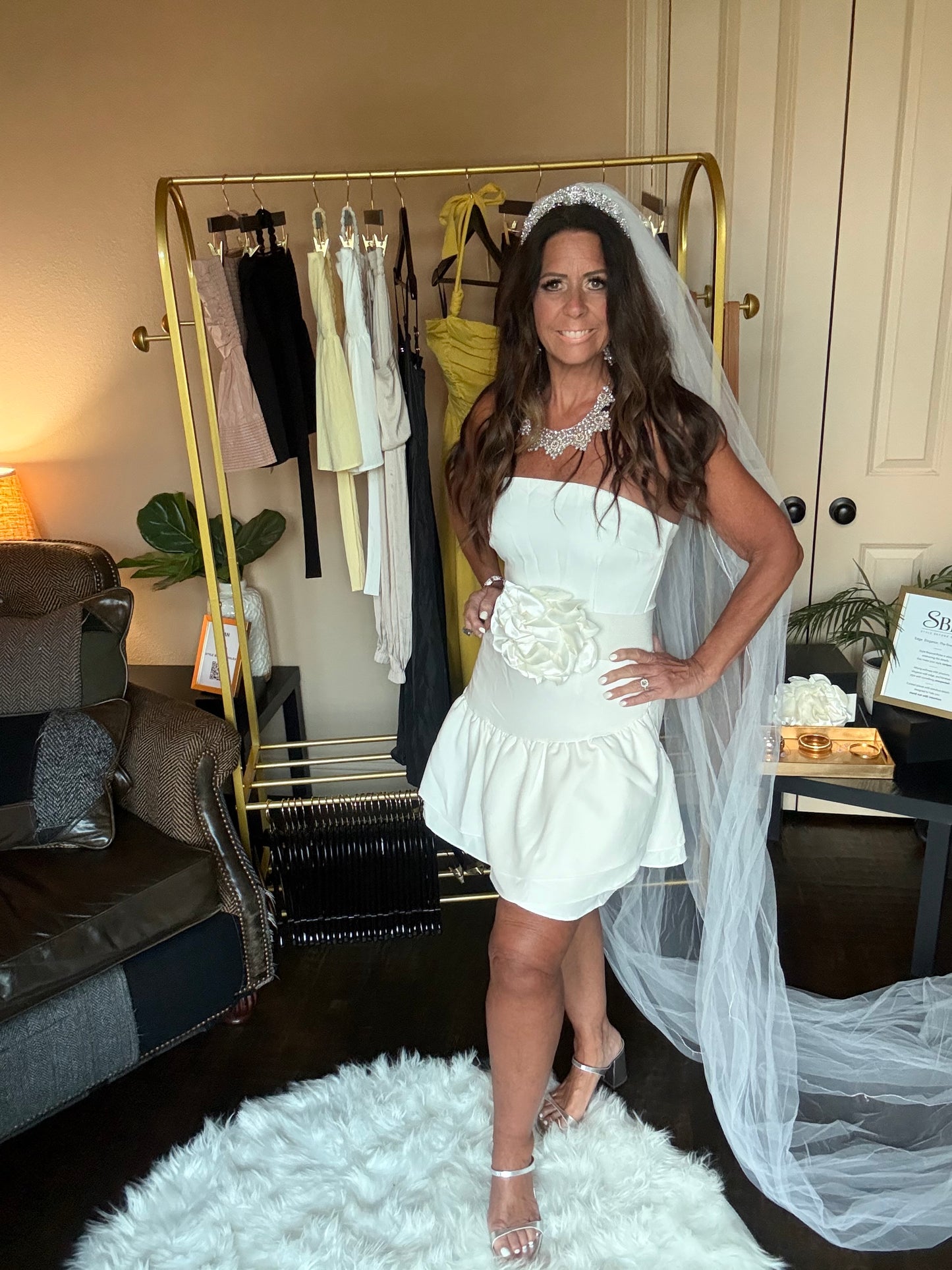 Woman in a white dress with a floral detail standing in front of a mirror.