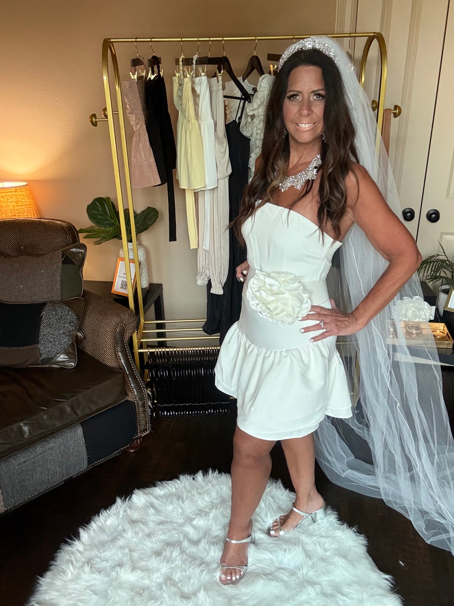 Woman in a white dress with a veil and bouquet standing in a room with furniture and decor.