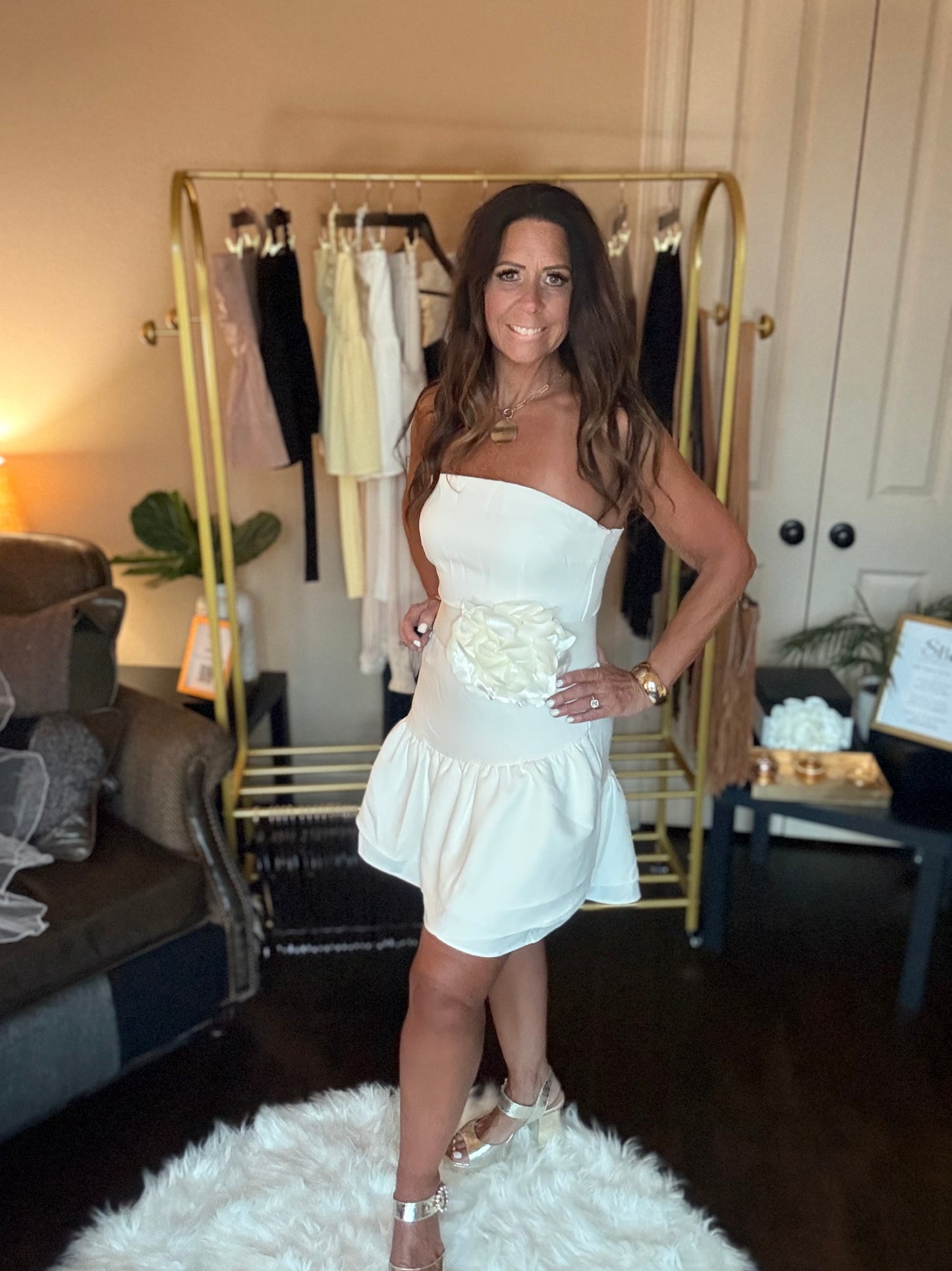 Woman in a white dress standing in a room with a clothing rack and decor.