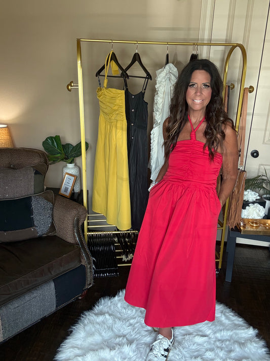 Woman in a red dress standing next to a rack of dresses in a room.