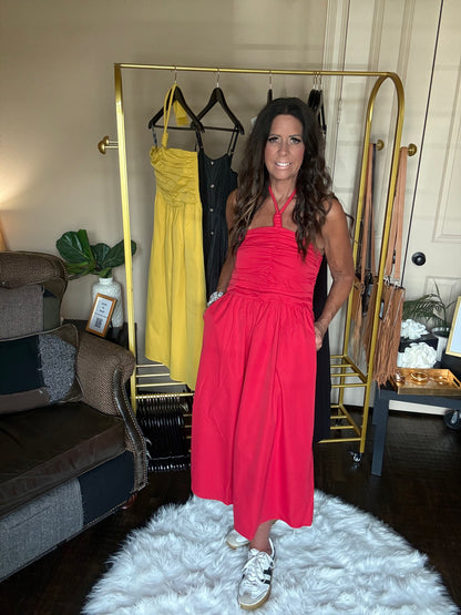 Woman in a red dress standing in a room with a gold rack and clothing.